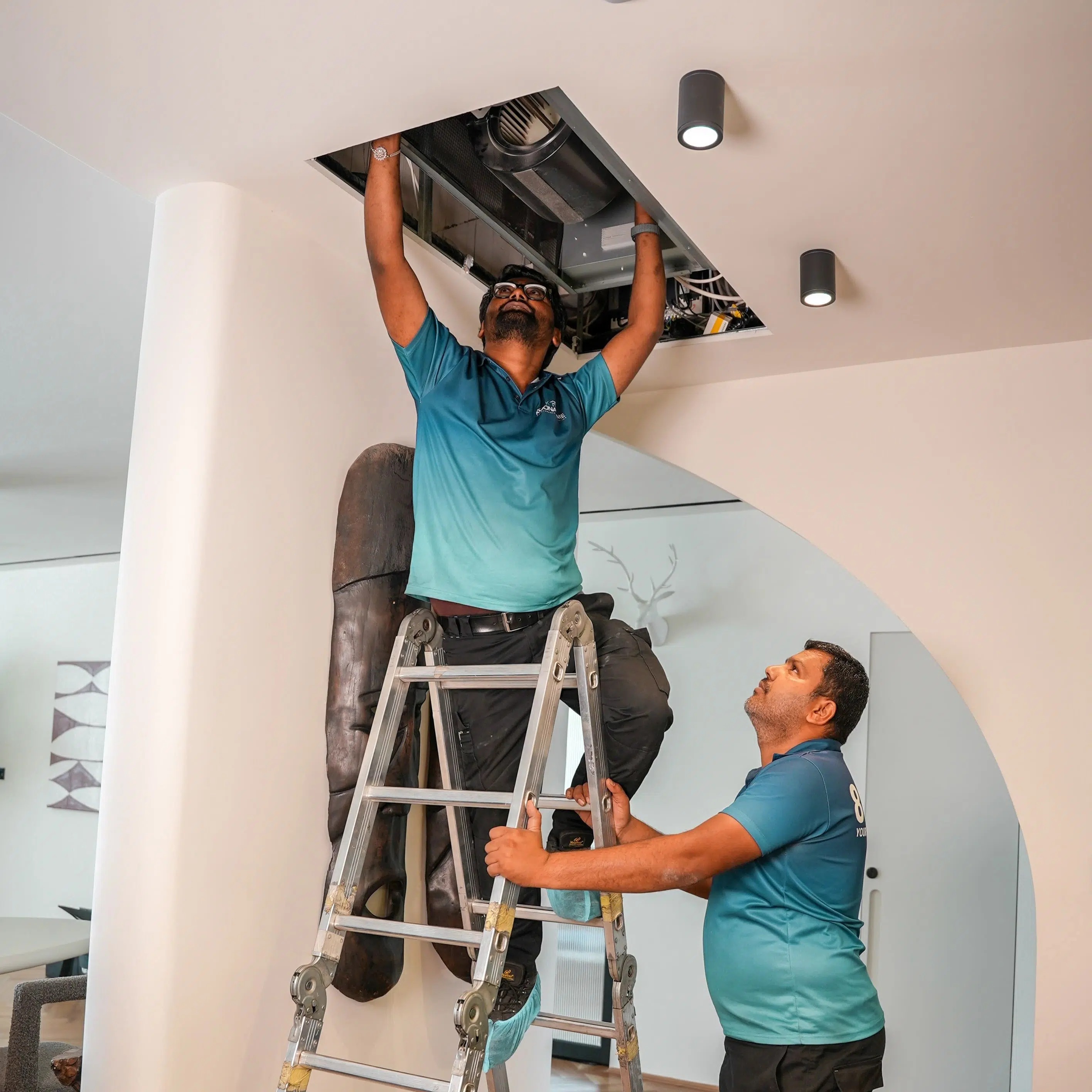 Technicians performing AC servicing and repair by Koona Home, maintaining a ceiling air conditioning unit indoors.