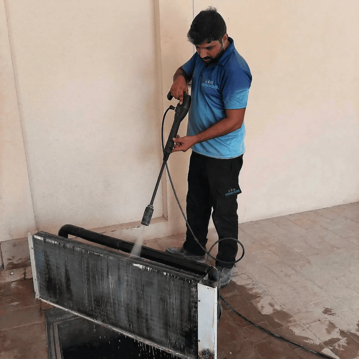 Coil Cleaning service in Dubai technician using a high-pressure washer to clean an AC coil unit, removing dirt and buildup in a maintenance area.