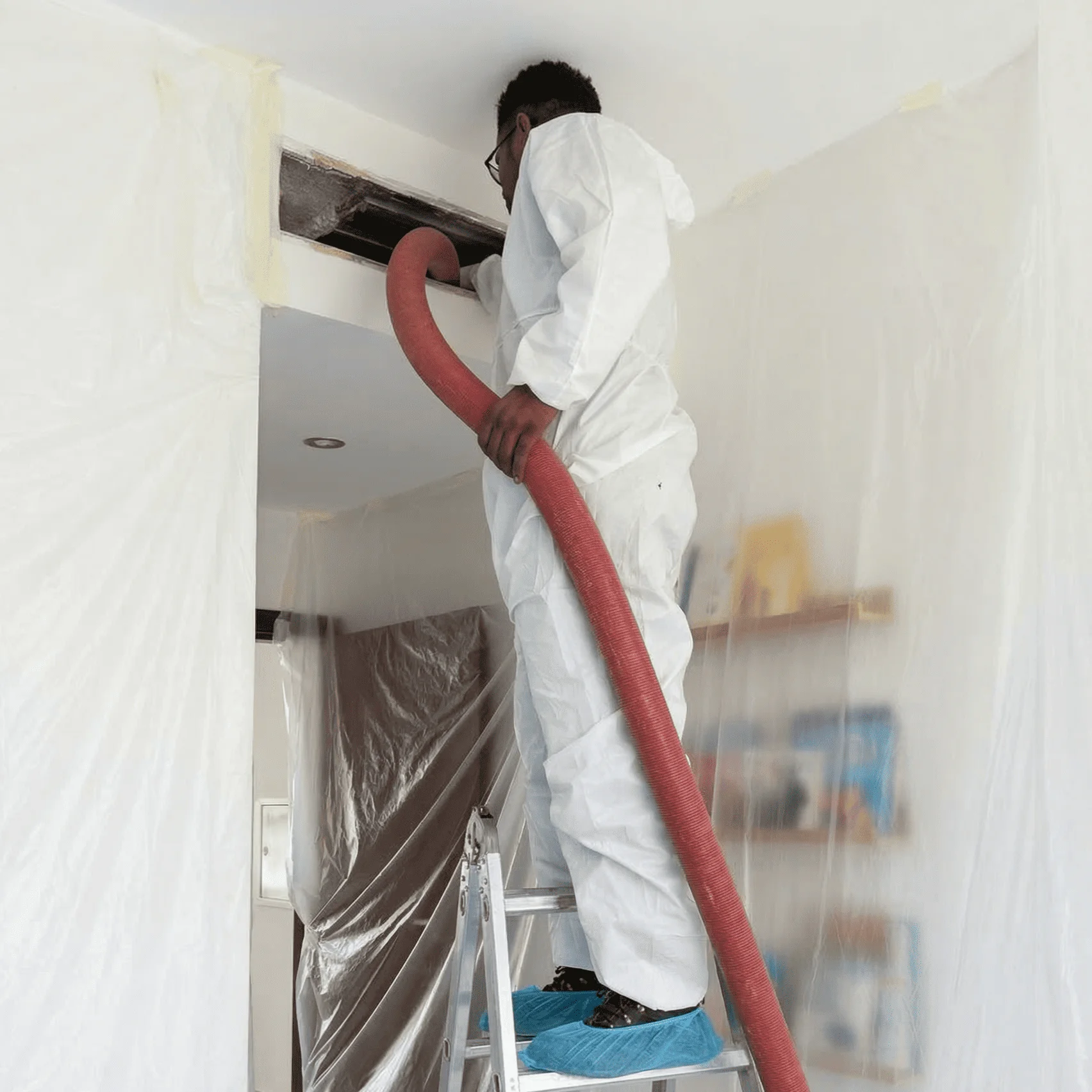 Duct cleaning service in Dubai technician wearing protective gear using a vacuum hose to clean air ducts through a ceiling vent inside a residential space.